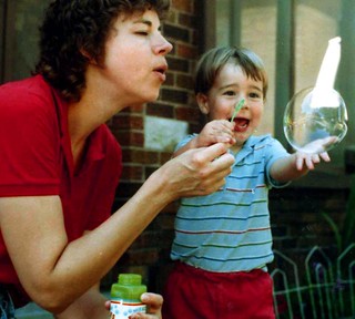 Adult and child blowing bubbles together; smiling child reaching for large bubble