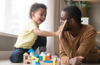 Toddler and adult playing blocks together in a house, smiling and giving each other a high five