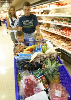 Two adults with children in a grocery store - children sitting in shopping car full of food