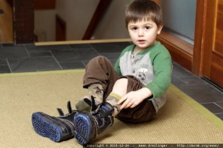 Young child sitting on the ground and putting on their boots