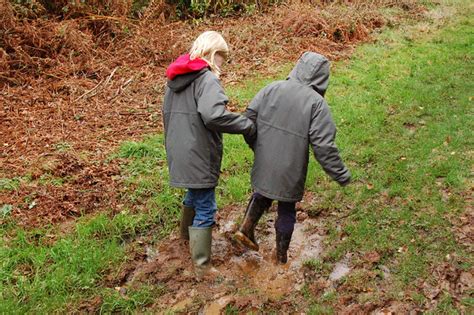 the backs of two people wearing rainjackets and boots, walking through mud