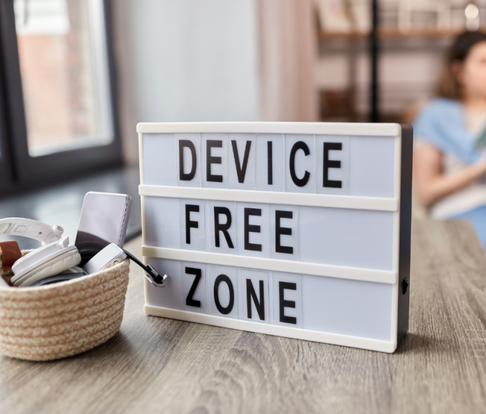 "Device Free Zone" sign on a table. Blurred picture of a person in the