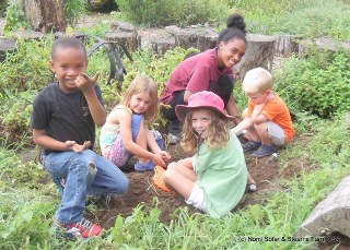 Four children and an adult sitting outside in nature - everyone smiling