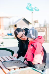 Educadtor and child outside in playground, by a bench, exploring materials