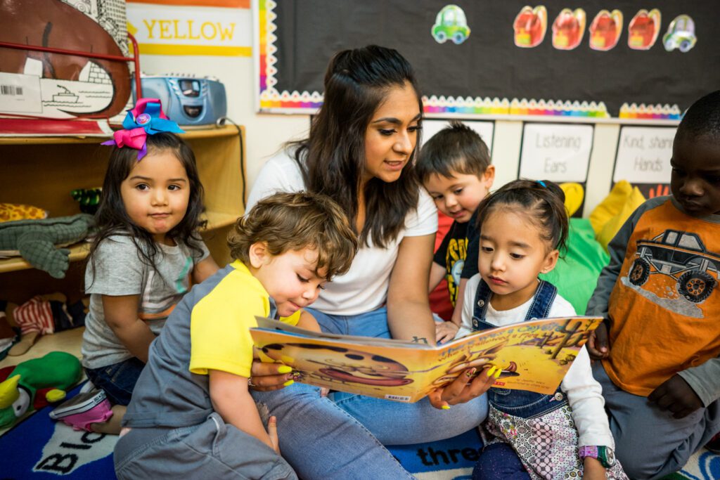 Children sitting with an educator on classroom carpet who is reading to them