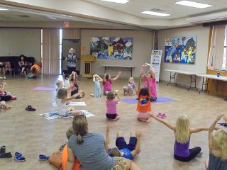 A group of children and adults stretching doing yoga indoors