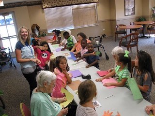 A long table with adults and children of various ages doing paper crafts together