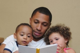 An adult in the middle of two children reading a book together