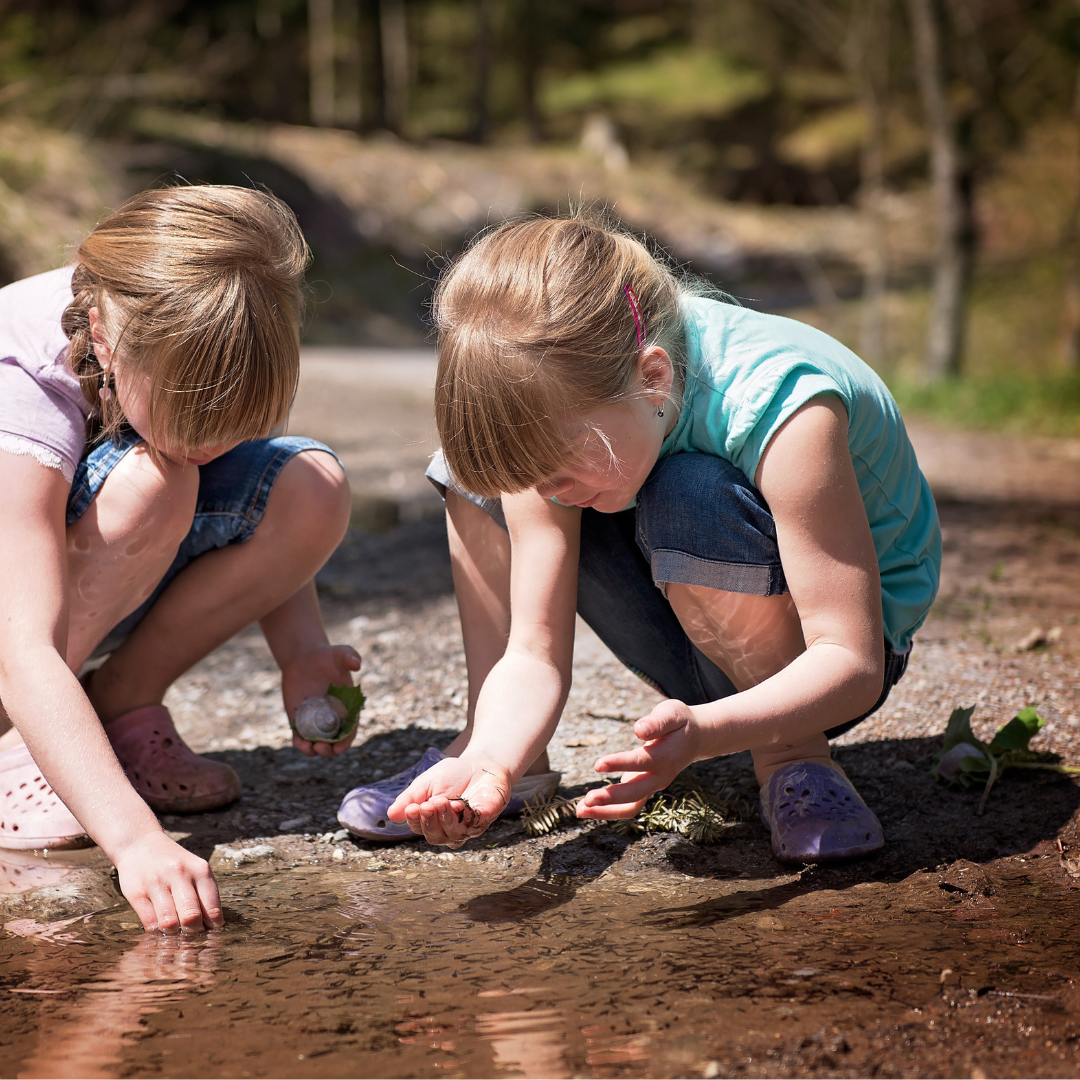 Two children crouched down at near shallow body of water in summer