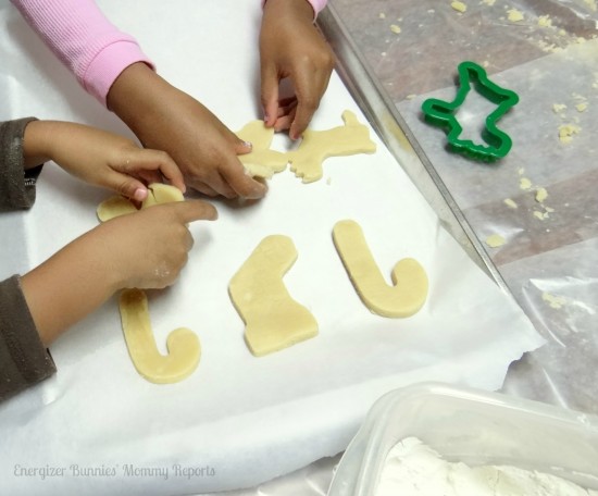 Two kids hands' putting cut out cookie dough shapes onto baking pan