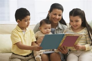 One adult reading with two school age children and a baby