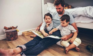 Parent reading to two young children sitting on bedroom floor 