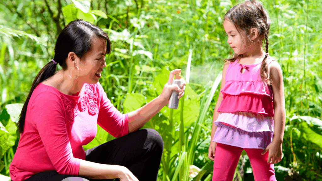 Adult spraying bug spray on child in the outdoors