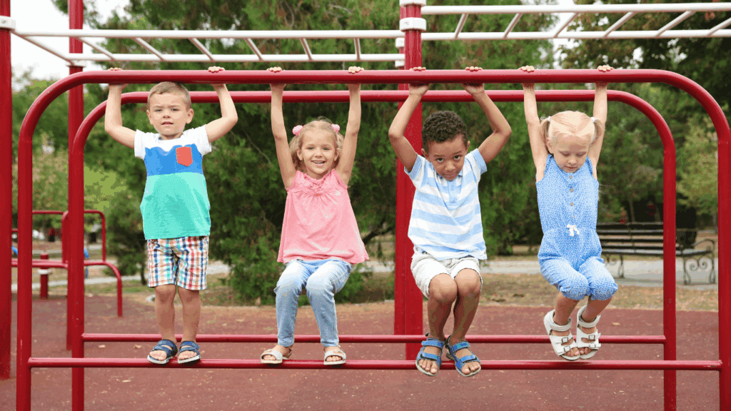 Four young children swinging on playground bars