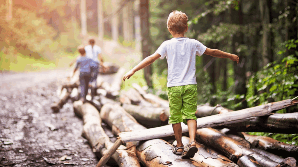 Three school age children balancing on tree logs outdoors