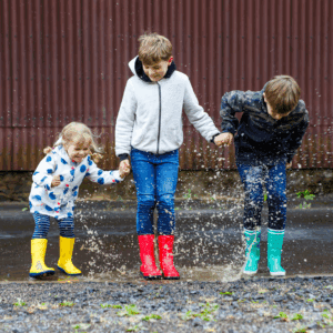 Three children of different ages holding hands and splashing in puddles.