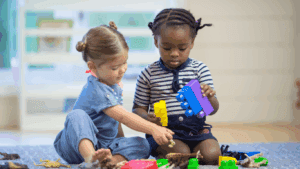 Two young children playing with blocks together inside