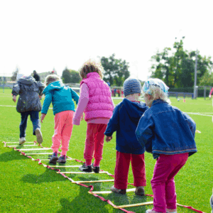 5 children jumping through an obstacle course outside on the grass