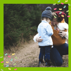 Parent wearing a baby carrier, holding a baby and comforting a toddler, outside in nature
