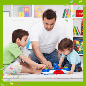 A parent kneeling on the floor between school age child and toddler, showing them a new toy