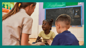 Kindergarten development: Two children sitting with educator in a classroom 