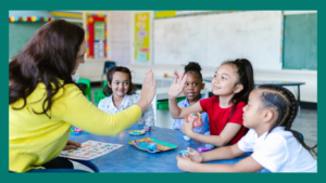 Teacher high fiving a child, sitting in a small group at a classroom table. 