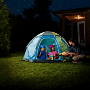Two kids in a tent outside with head lamps; adult kneeling down and offering snacks